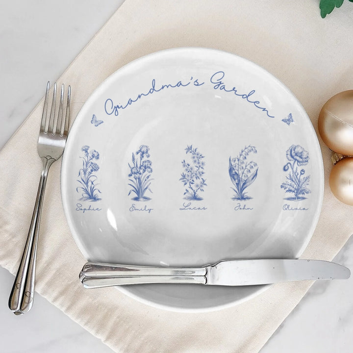 Custom toile birth flower ceramic plate with personalized title, names, butterflies, and floral motifs in blue, on table-ARTFULANE