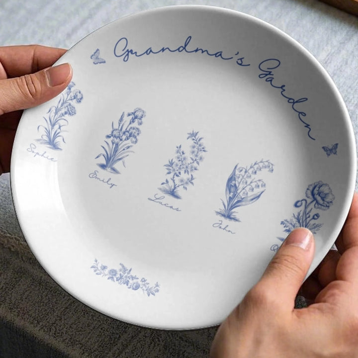 Custom toile birth flower ceramic plate with personalized title, names, butterflies, and floral motifs in blue, in hands-ARTFULANE